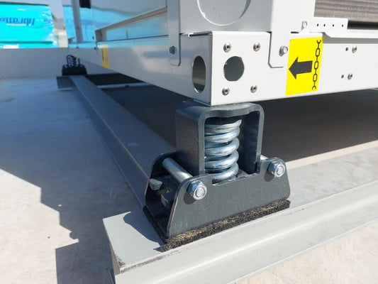 Close-up of a vibration isolator consisting of a spring held inside a steel bracket, supporting a piece of mechanical equipment on a metal frame.