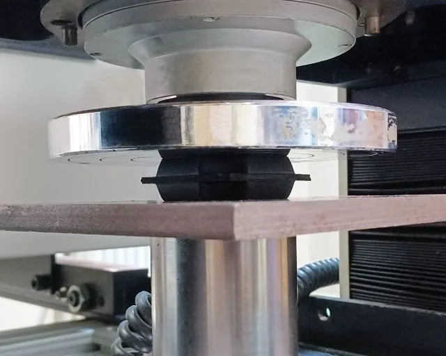 Mechanical testing machine applying pressure to a black rubber component.