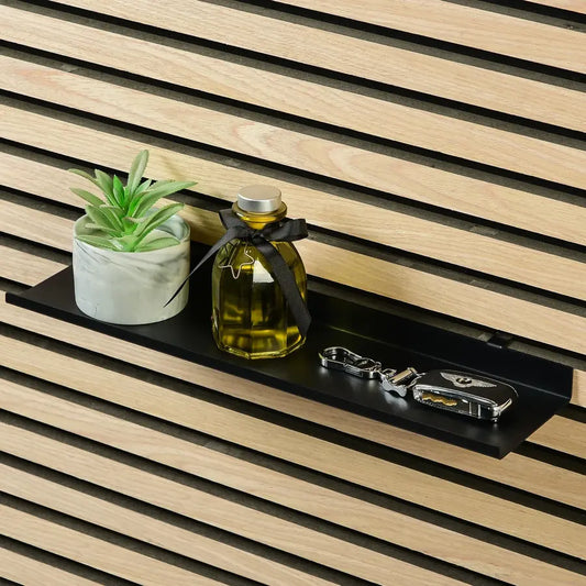 A small black shelf holds a potted plant, an aromatherapy bottle, and a set of keys. The shelf is mounted on a wooden slat wall.
