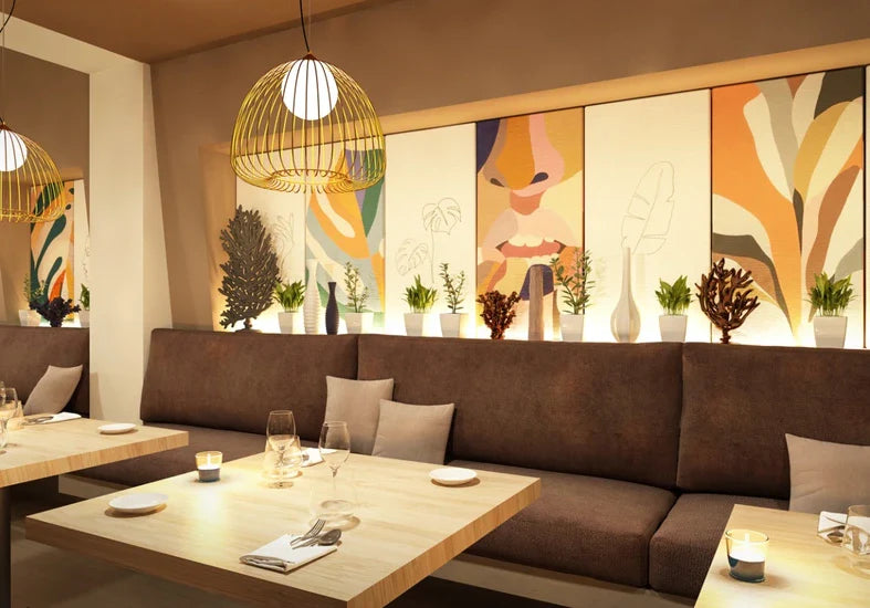 Restaurant interior with brown banquette seating, light wood tables, and modern gold pendant lighting. Artwork panels and plants decorate the space.