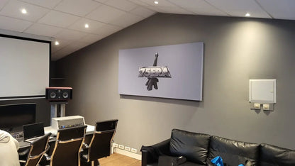 Interior of a room with audio equipment, a projector screen, a black leather sofa, and a framed logo on the wall.