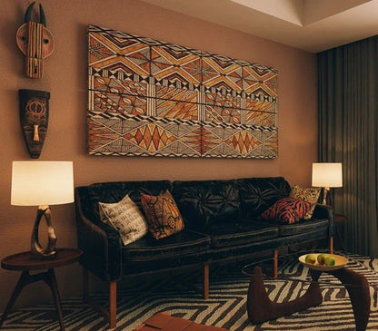 A living room with a black leather sofa, colorful pillows, a patterned rug, and tribal art on the wall.