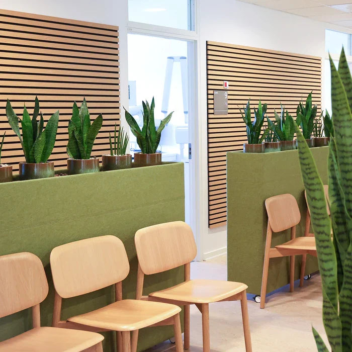 Waiting room with wooden chairs, green partitions with potted plants, and slatted wooden walls.
