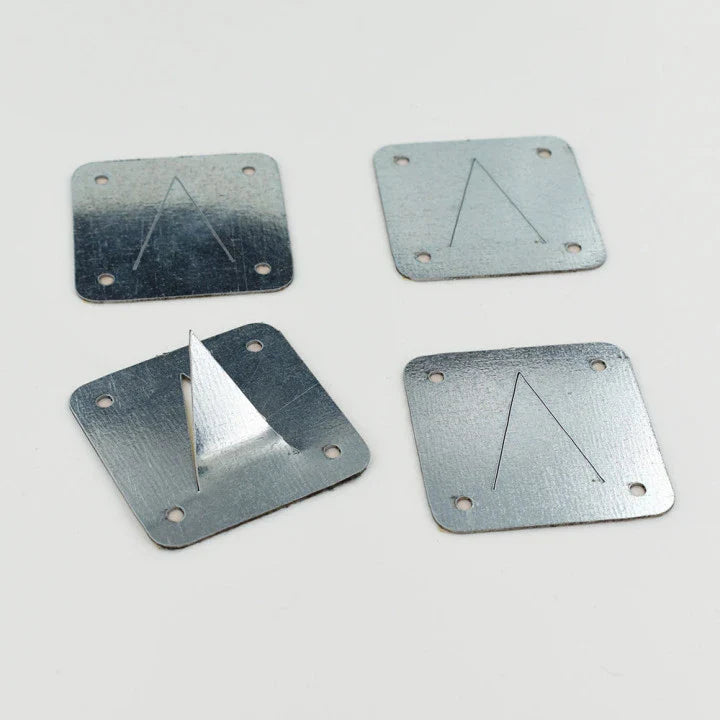 Four square metal plates with a triangle cut into them and a hole in each corner. One plate has the triangle bent upward.