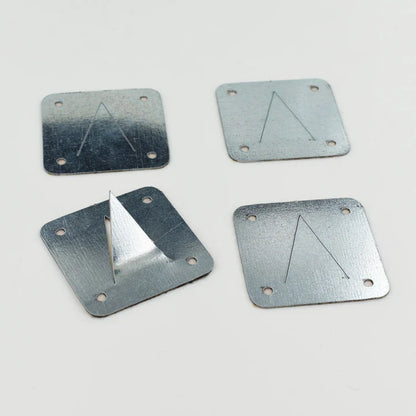 Four square metal plates with a triangle cut into them and a hole in each corner. One plate has the triangle bent upward.