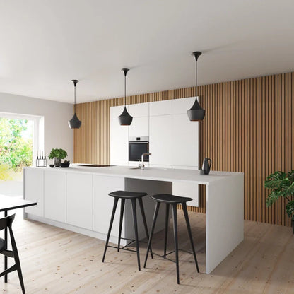 A modern kitchen with white cabinets, a long white island, black stools, and three black pendant lights.