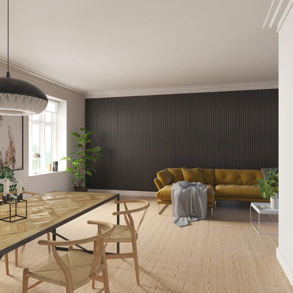 Well-lit living and dining area with a mustard-colored sofa, wooden dining table, and matching chairs against a dark gray paneled wall and light wood flooring.