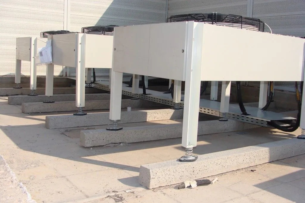 Several large, white industrial air conditioning units sitting on concrete blocks on a flat roof.
