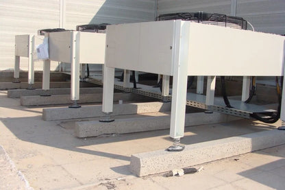 Several large, white industrial air conditioning units sitting on concrete blocks on a flat roof.