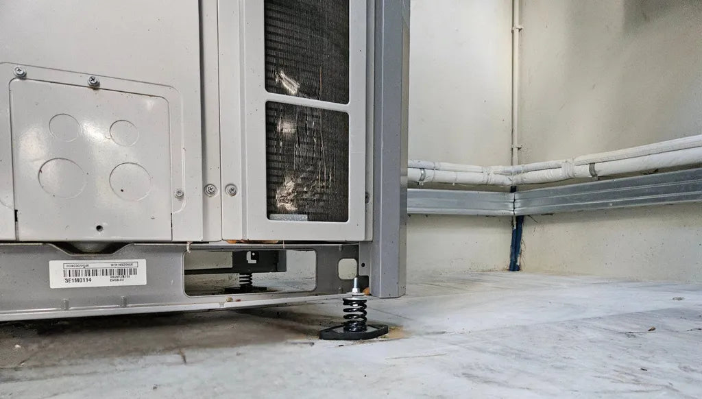 Air conditioning unit with spring mounts on a concrete floor.
