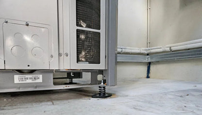Air conditioning unit with spring mounts on a concrete floor.
