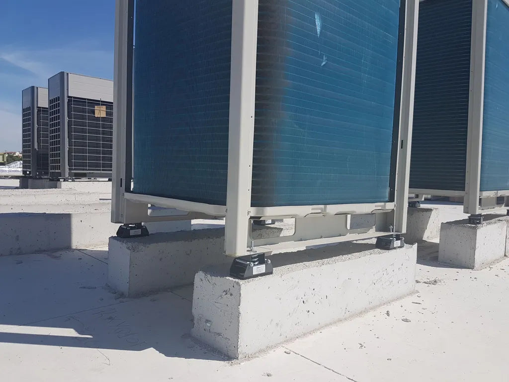 Multiple large, blue air conditioning units sitting on concrete blocks on a roof.