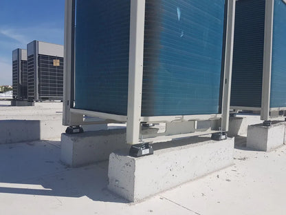 Multiple large, blue air conditioning units sitting on concrete blocks on a roof.