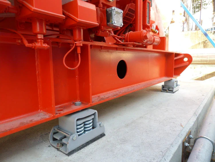 Large, red industrial machinery supported by grey spring vibration isolators on a concrete foundation.
