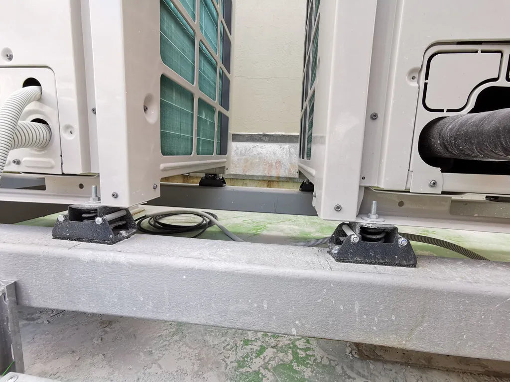 Close-up of air conditioning units on a metal frame, each supported by a black rubber mount with a visible bolt.