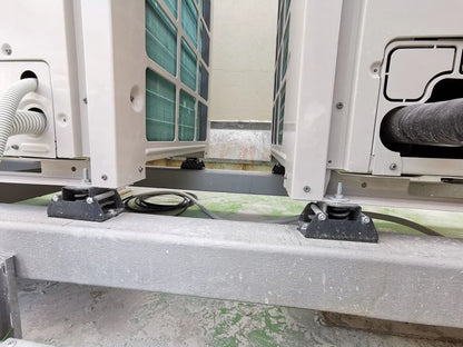 Close-up of air conditioning units on a metal frame, each supported by a black rubber mount with a visible bolt.