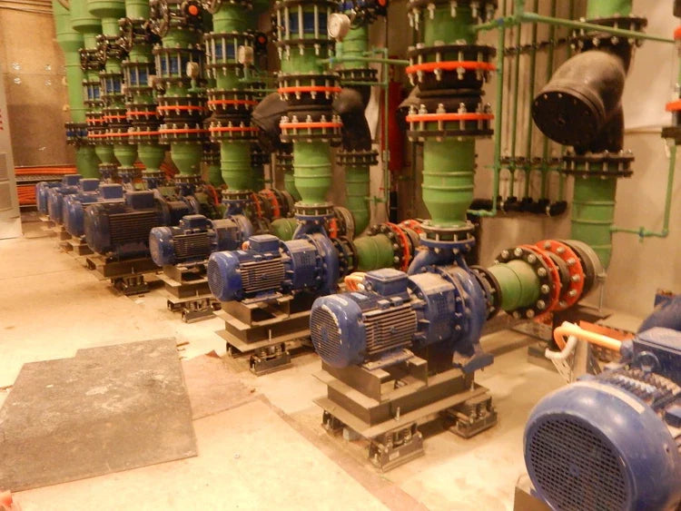 Rows of blue industrial pumps and green pipes with orange connectors in a mechanical room.
