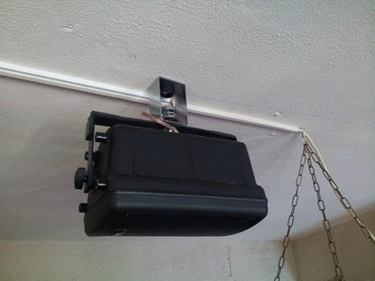 A black, boxy loudspeaker mounted to a white ceiling track.