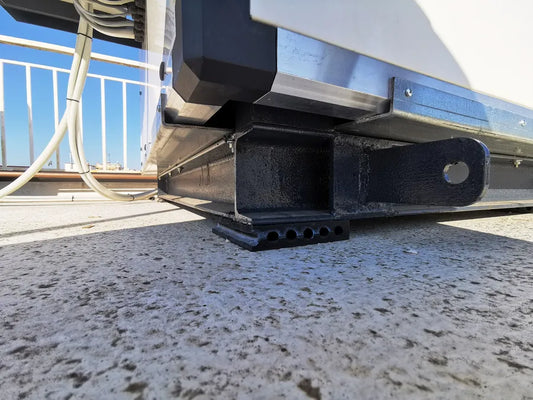 Close-up of a black metal frame with a tow hitch and ventilation holes, resting on a weathered concrete surface outdoors.