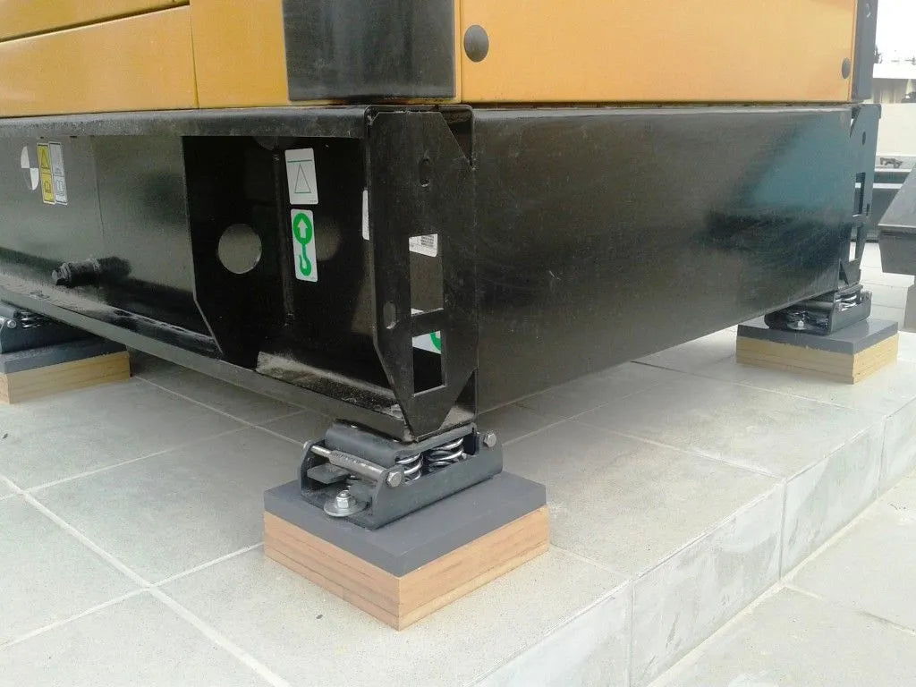 Close-up of black machinery supported by vibration isolation mounts on a tiled surface.