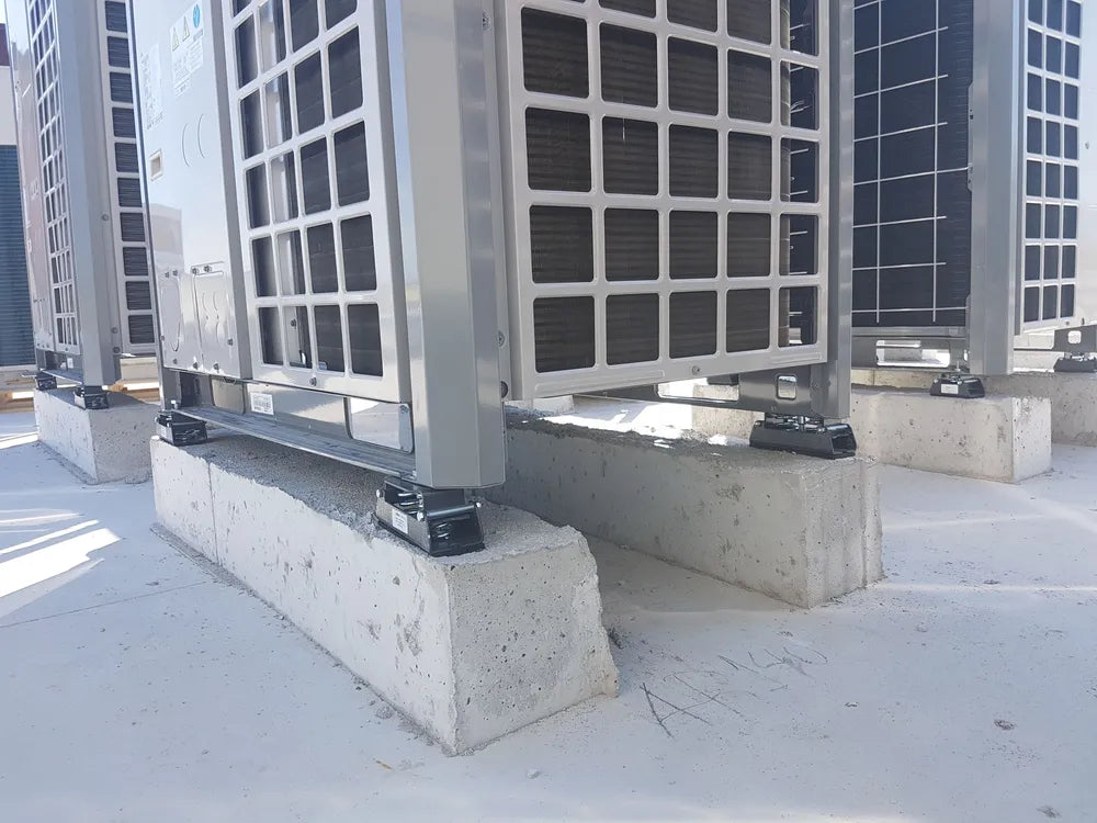 Several air conditioning units are installed on concrete blocks on a flat, white surface.