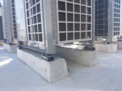 Several air conditioning units are installed on concrete blocks on a flat, white surface.