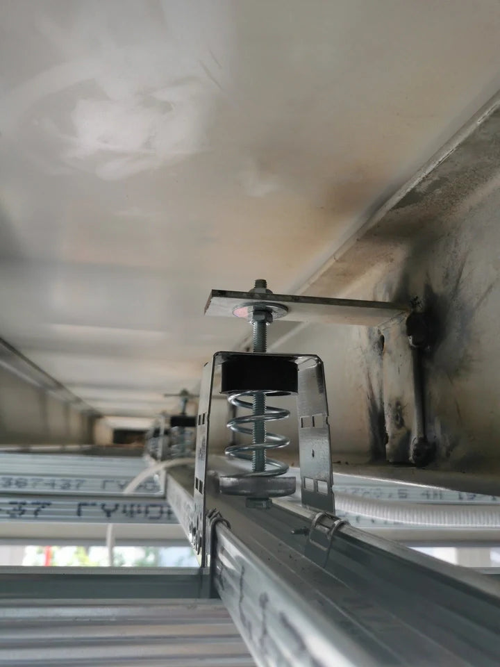A close-up view looking up at a metal framework with a spring dampener attached to a ceiling.