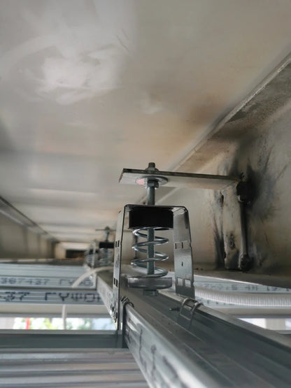 A close-up view looking up at a metal framework with a spring dampener attached to a ceiling.