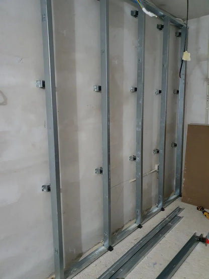 Metal studs attached to a wall, with track lying on the floor.