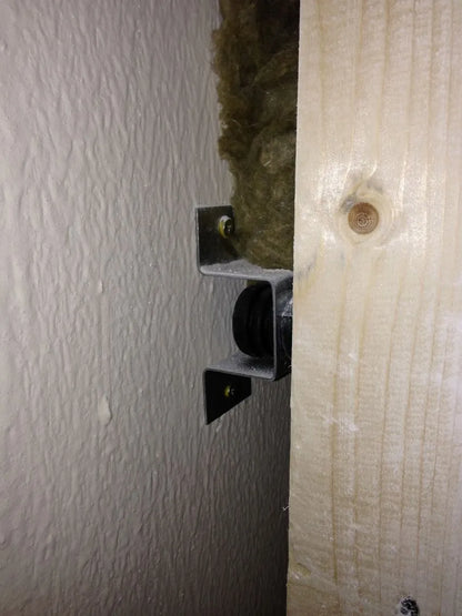 Close-up of a bracket supporting a black pipe with insulation and wallboard.