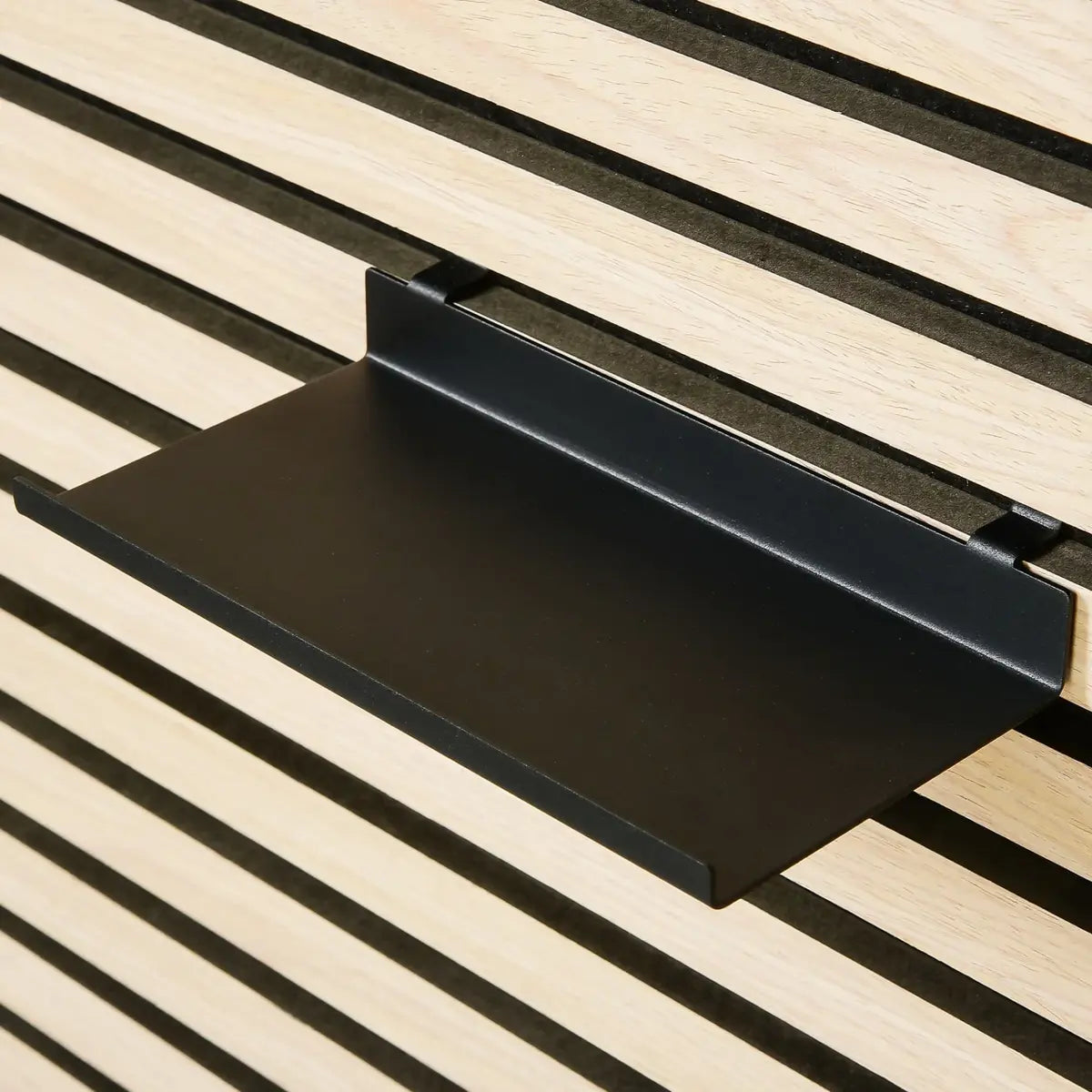 Close-up of a black metal shelf attached to a wooden slatted wall.
