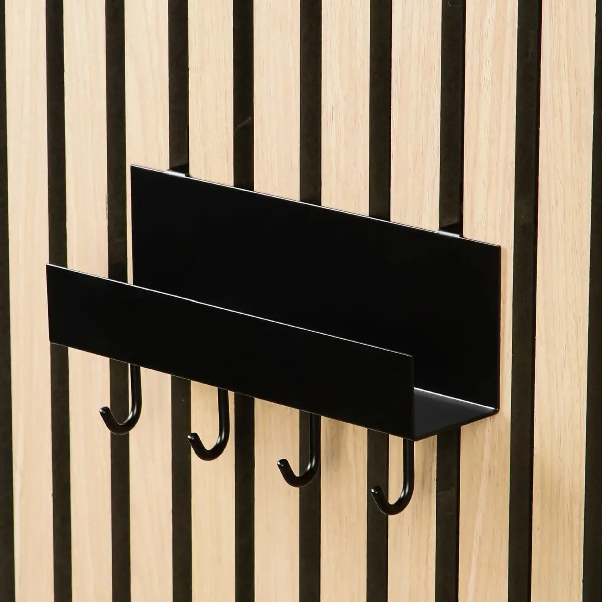 Black metal wall shelf with hooks attached to a wood slat wall.