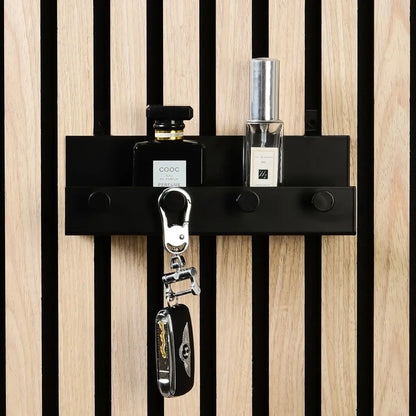 A black shelf with perfume bottles and keys hanging on a wall with vertical wood slats.
