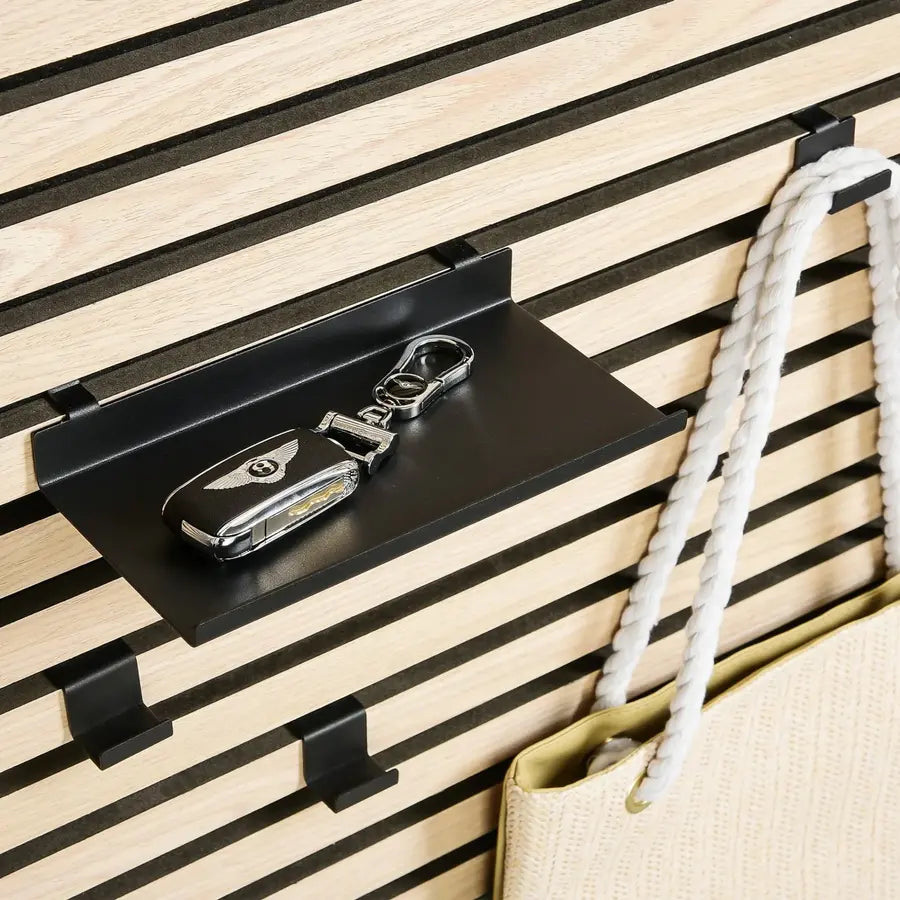 A Bentley key fob on a black shelf mounted on a slatted wall, next to a beige bag with white rope handles.
