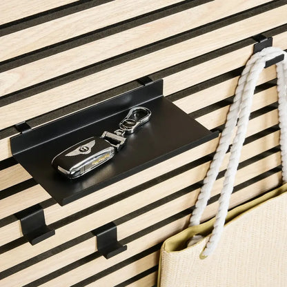 A Bentley key fob on a black shelf mounted on a slatted wall, next to a beige bag with white rope handles.
