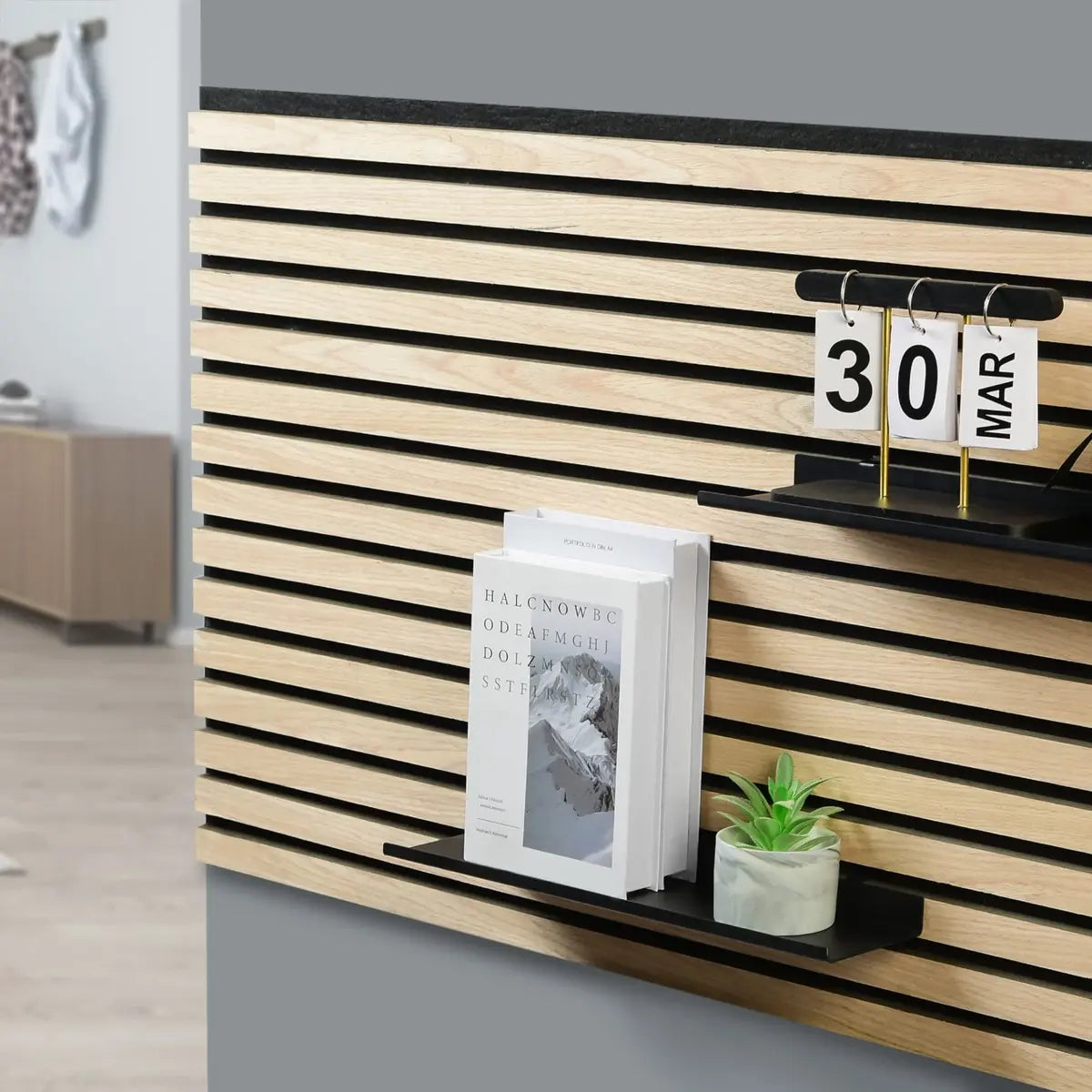 Close-up of a wooden slat wall with black accents, featuring a book, a small succulent, and a calendar set to March 30th.