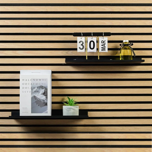 A calendar, bottle, book, and plant on black shelves against a striped wooden wall.