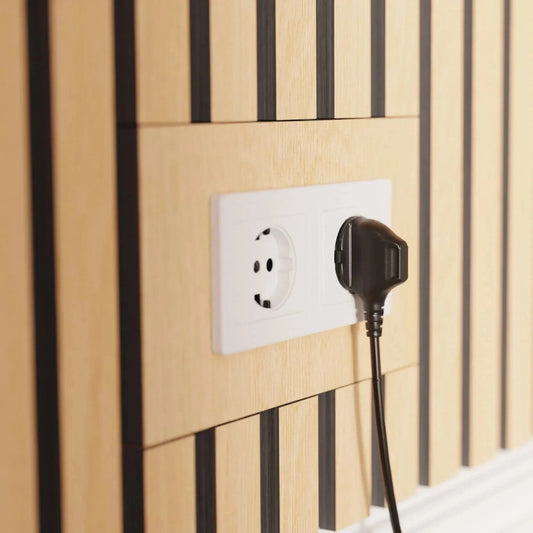 A black plug inserted into a white electrical outlet on a light brown and black wood paneled wall.